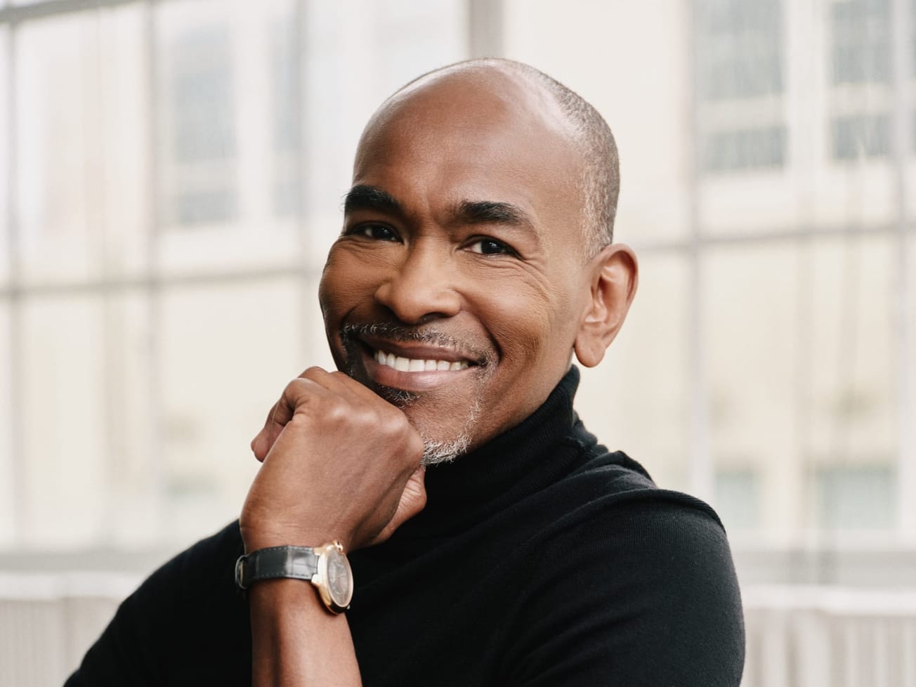 Person with short hair wearing a black top and a wristwatch, resting their chin on their hand