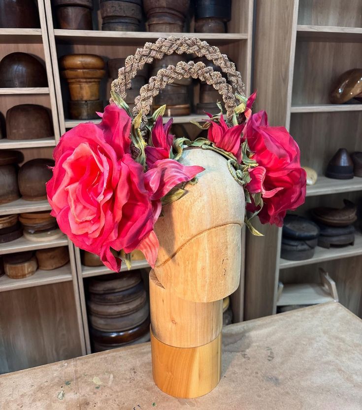 Braided headpiece with two large artificial pink flowers displayed on a wooden mannequin head