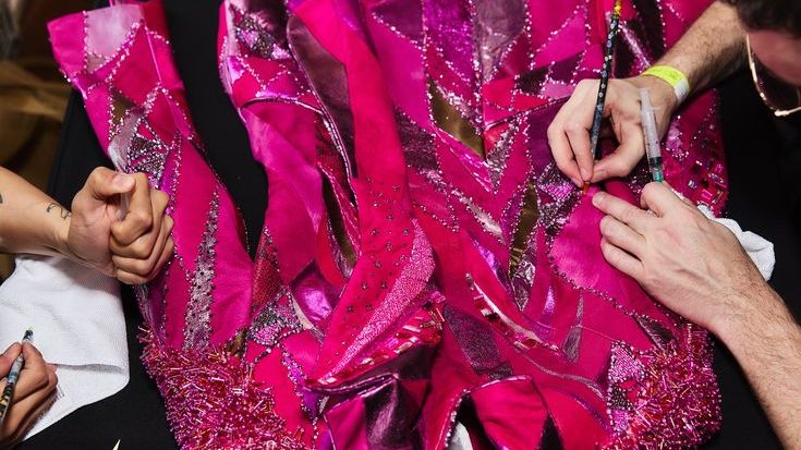 Hands working on a detailed pink garment with sequins and bead embellishments
