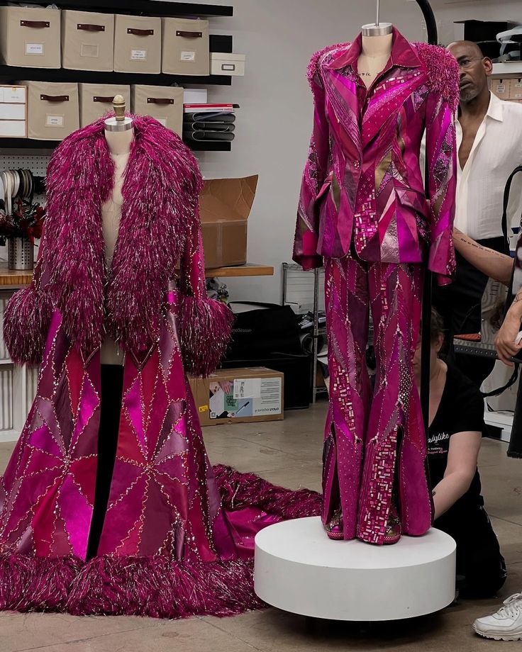 Two mannequins display matching pink outifts with feathered accents, one a long coat and the other a suit with flared pants