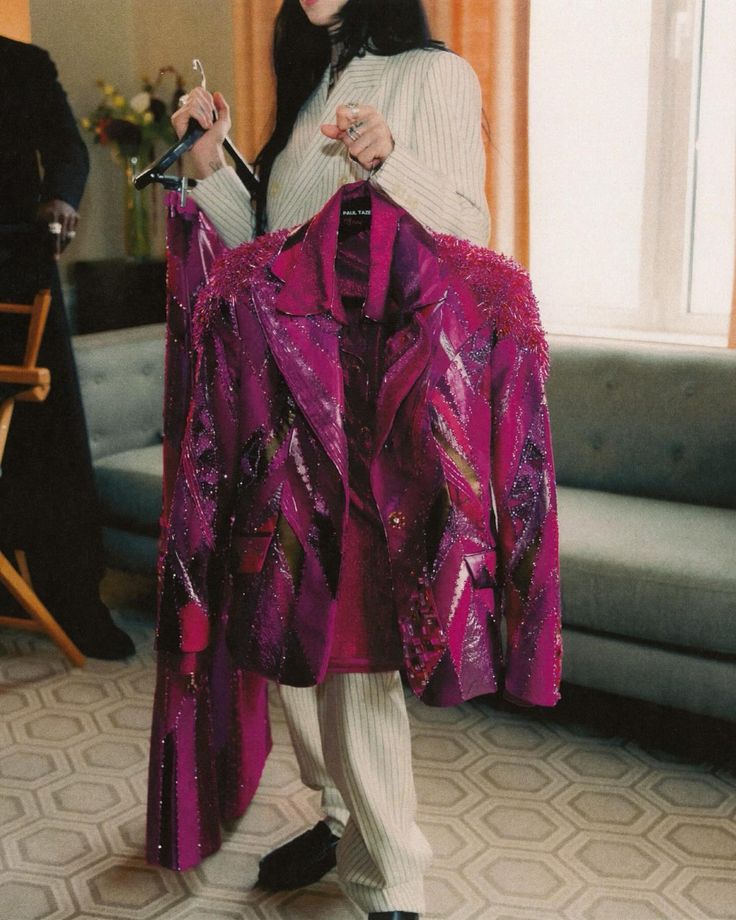 Person holding two sequined jackets on hangers in front of a sofa