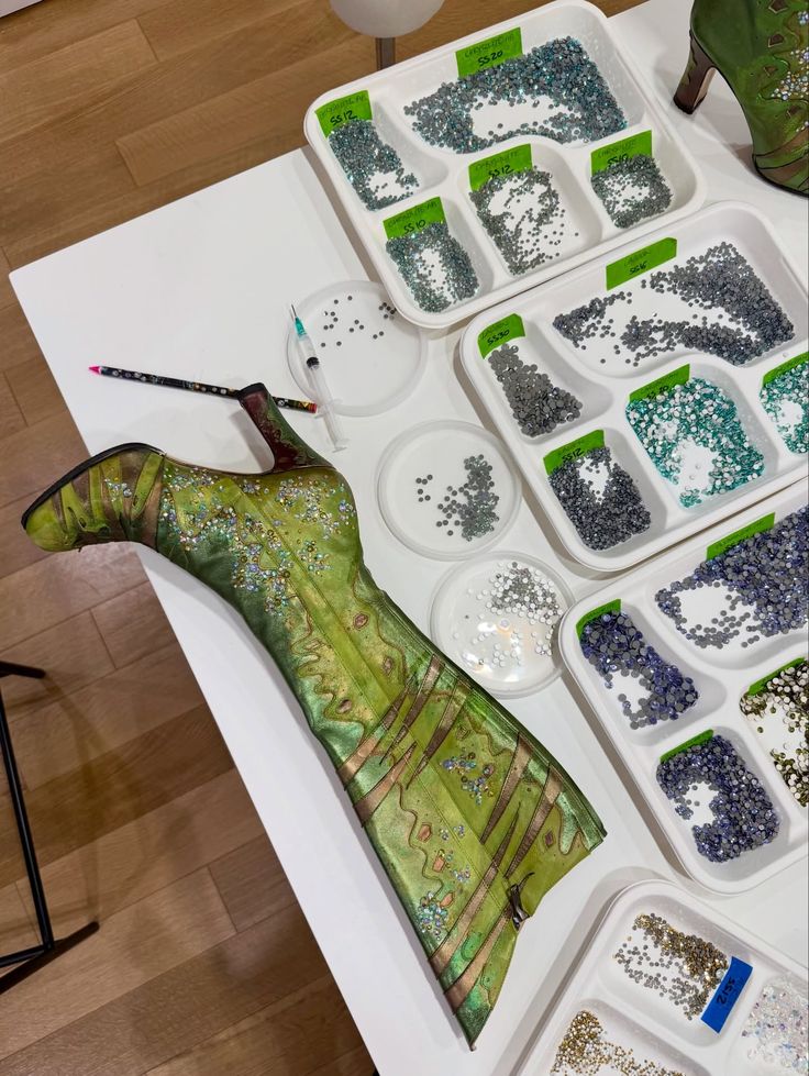 Green high-heeled shoe with scattered beads next to trays containing multiple compartments of sorted beads in various colors