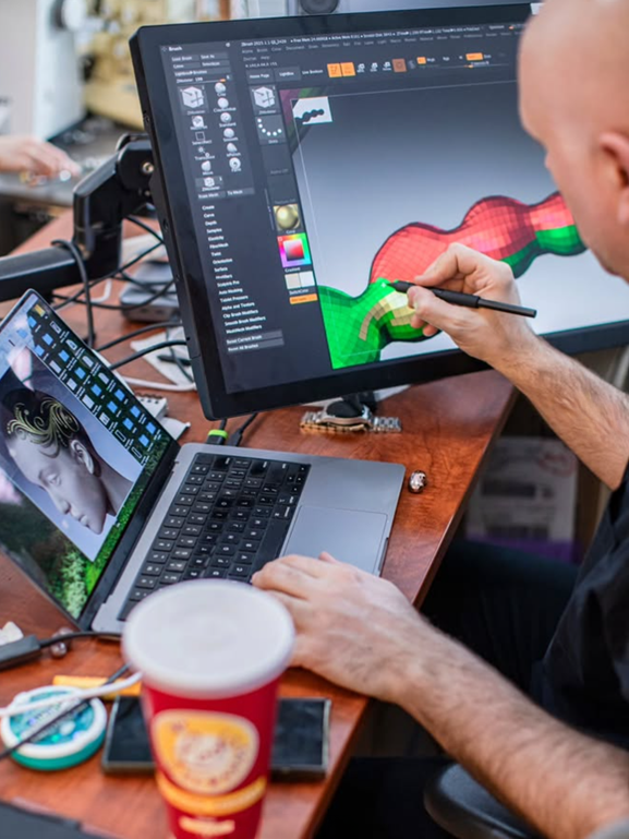 Person using a stylus on a touchscreen laptop displaying a 3D modeling software with a colorful 3D project