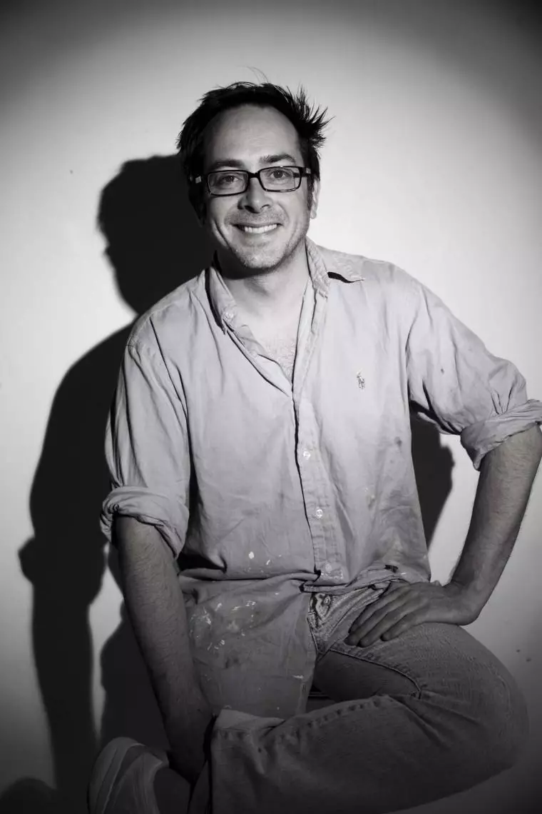 Person sitting with one knee up and hand resting on it wearing a long-sleeve shirt with rolled-up sleeves and pants