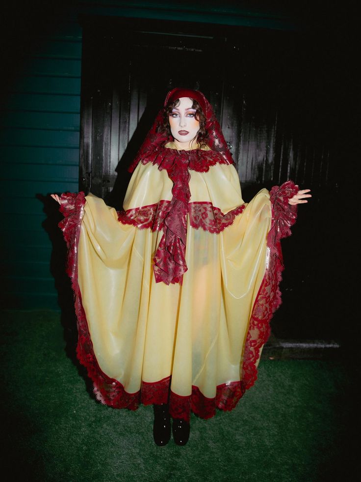 Person wearing a flowing yellow garment with wide sleeves and red lace trim standing with arms extended