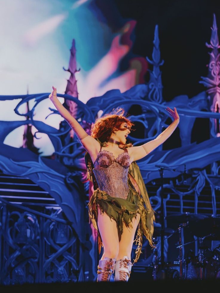 Woman in theatrical costume with arms raised standing on stage