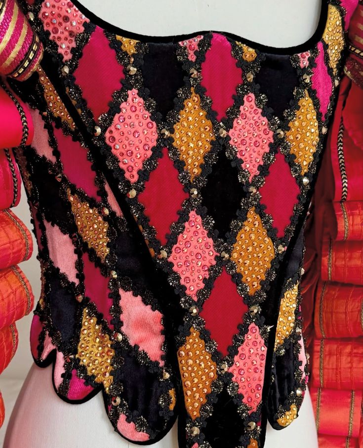 Close-up of a garment with a harlequin pattern of diamond shapes embellished with small beads and black lace trim
