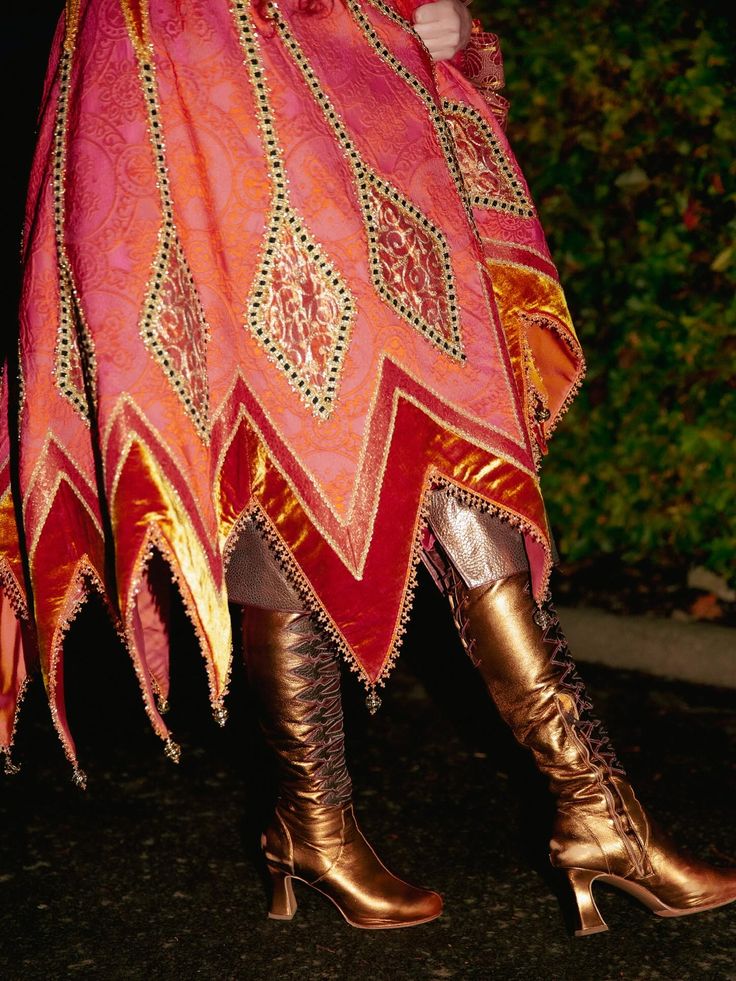 Person wearing a patterned poncho with jagged edges and metallic knee-high lace-up boots