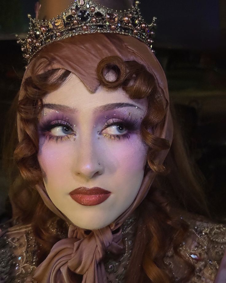 Person wearing a jeweled crown and an ornate garment with embroidery and embellishments