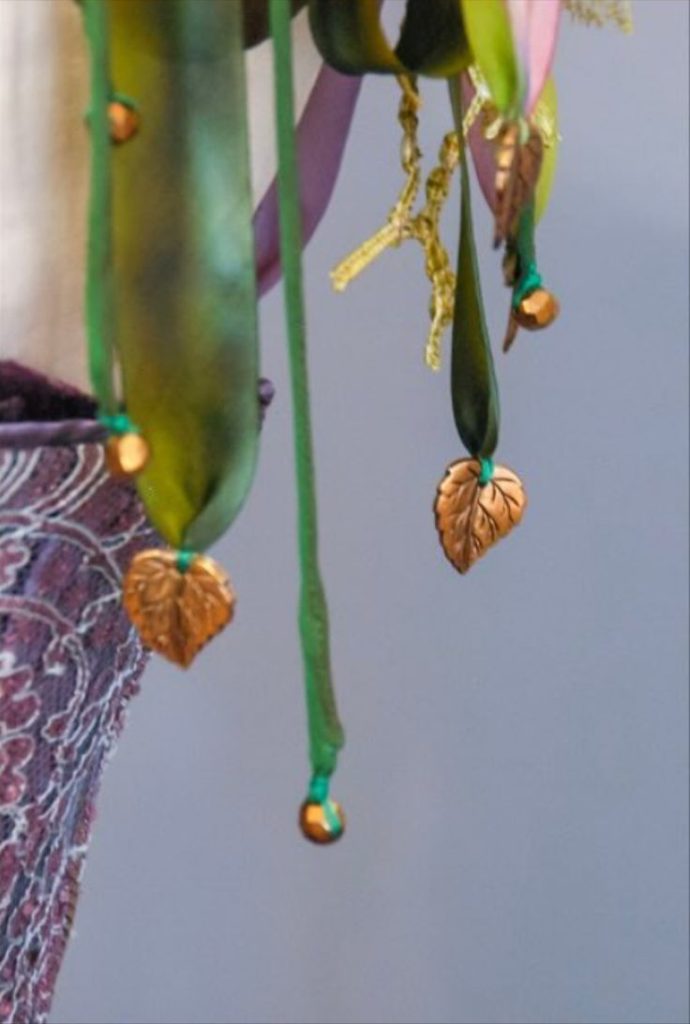 Close-up of hanging decorative elements including leaf-shaped pendants and beads on green ribbons against a plain background