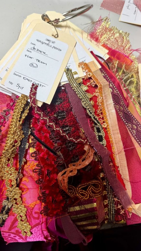 Collection of fabric swatches with various trims and embellishments attached to a metal ring with a label tag