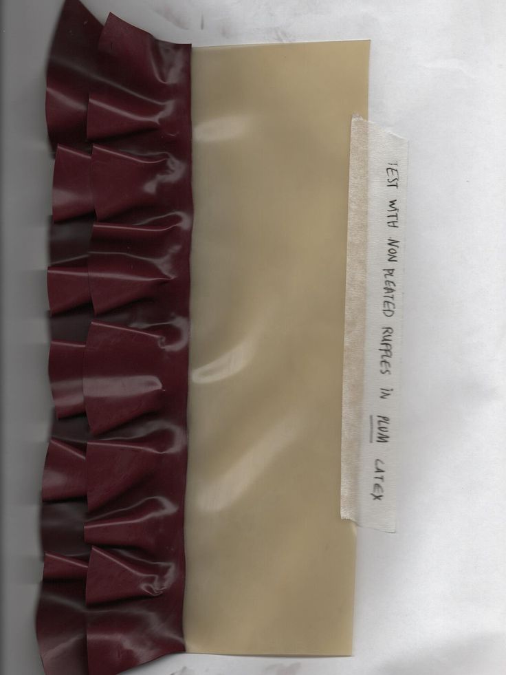 Fabric sample with pleated dark red strip attached to a beige bae and a typed label reading "TEST WITH NON PLEATED RUPPLES IN PLUM LATEX"