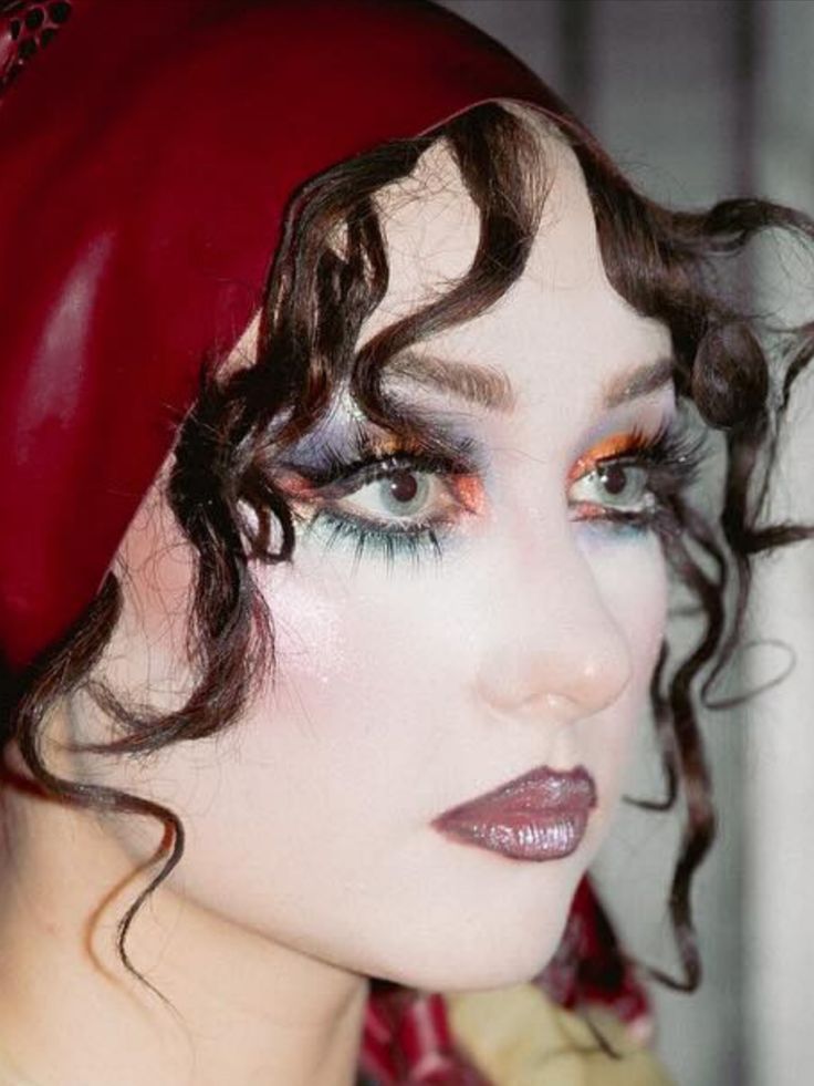 Side profile of a person with long curly hair wearing make up and long lashes and a red headpiece covering the top of their head