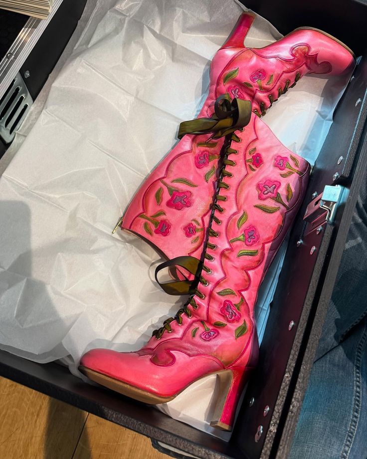 Pair of pink high-heeled boots with floral embroidery and brown laces inside a box