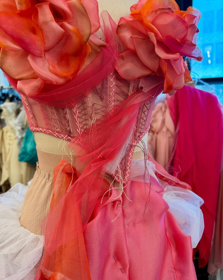 Back view of a pink corset dress with large fabric flowers and tulle details on a mannequin