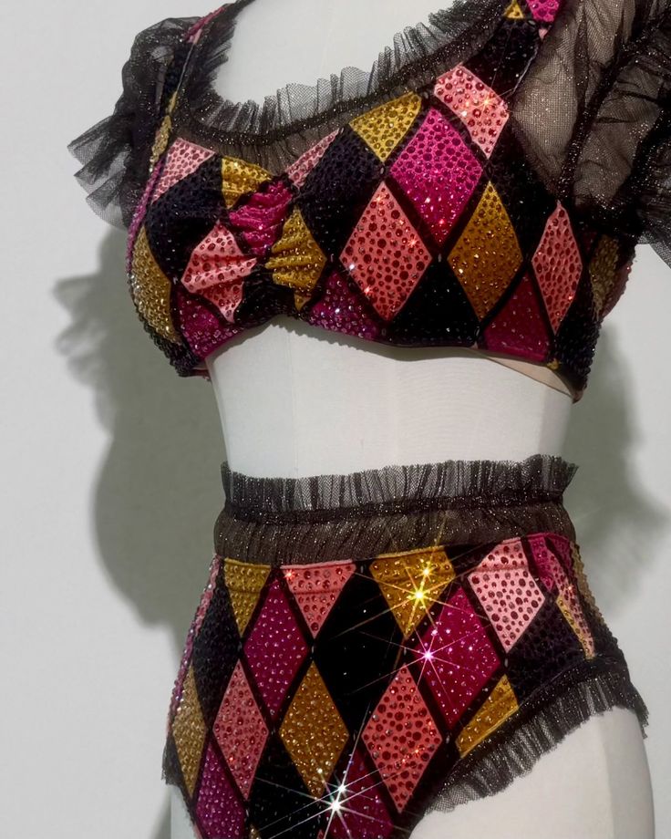 Two-piece outfit with diamond pattern in pink, gold, and black sequins and black sheer ruffled trim on sleeves, neckline, waist, and leg openings