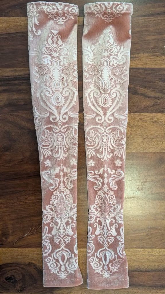 Pair of long, narrow fabric sleeves with a raised floral and ornamental pattern laid flat on a wooden surface
