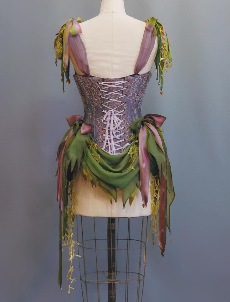 Back view of a corset with lace-up closure, decorated with green and purple fabric draped and tied with ribbons, displayed on a dress form